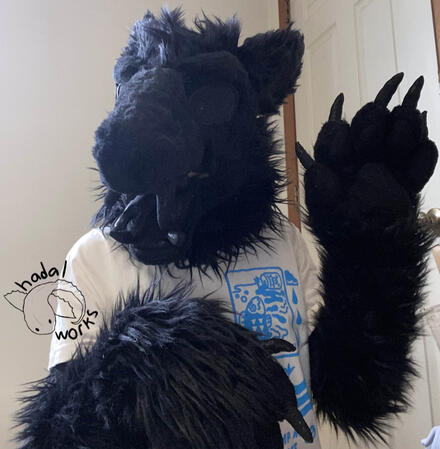 A fully black partial fursuit looking at the camera and waving a large pitch black paw.